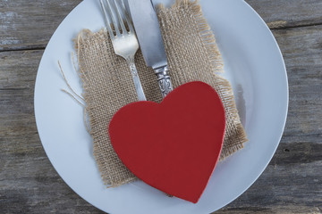 Table setting/red wooden heart and cutlery on white plate and old wooden background
