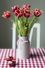 Rot-weisse Tulpen - Tulipa - in einem grauen Krug aus Keramik mit niederlaendischen Holzclogs dekoriert, auf einem Tisch. Farbwelt: gruen, rot, weiss, grau
