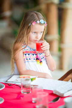 Little kid having breakfast at outdoor cafe. Adorable girl drinking fresh watermelon juice enjoying breakfast.