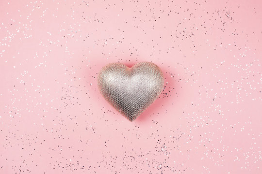Silver heart on pink background with sparkles.