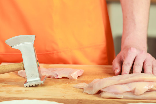 Man beating chicken meat on wooden board