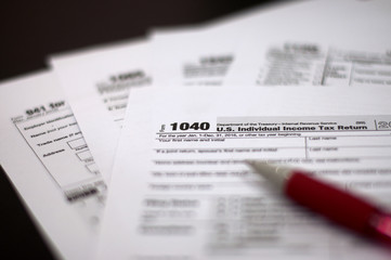 Tax Season: Horizontal left side view of 1040 U.S. Individual Income Tax Return Form with an office laptop background with red white pen and eye glasses foreground