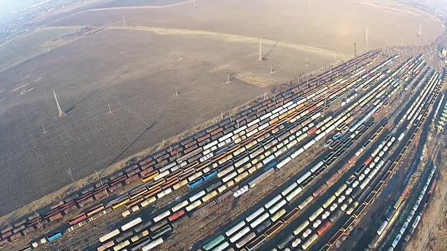 Many rows of colored freight train cars and oil tanks with petrochemical products  stationed on several railroad tracks of an industrial train depot terminal ,waiting for delivery, aerial view
