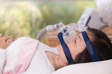 Sleep apnea therapy, Woman sleeping in bed wearing CPAP mask.Happy and healthy senior woman sleeping deeply on her back quietly without snoring,blurred CPAP machine background