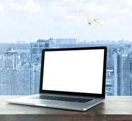 Laptop with blank screen on table against cityscape background. Wholesale and logistics concept