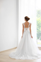 Bride in a beautiful wedding dress standing near window