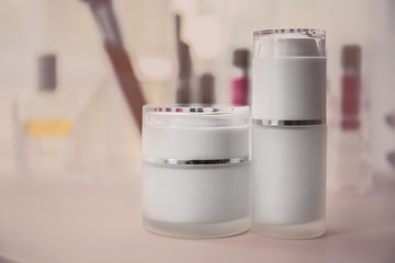 Bottle and jar of cream on white table against blurred background, close up view