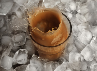 Glass of cold coffee with ice cubes and splashes on table