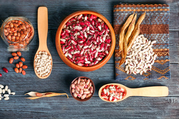 Assortment of haricot beans in bowls and spoons on dark wooden background