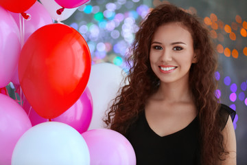 Beautiful African American woman with air balloons on blurred lights background