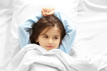 Funny little girl lying in bed at home