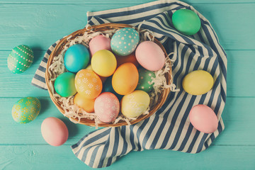Wicker basket with colourful Easter eggs on blue wooden background