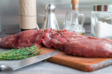 Raw red beef tender loin on wooden kitchen board with green and pink pepper and thyme. Selective focus.