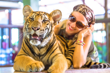 Smiling beautiful woman with sunglasses, embraces a little tiger, Panthera Tigris, sitting in Thailand. Concepts of courage, fun and dangerous.
