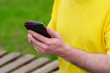 man holds phone and sits on a bench in Park