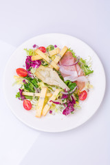 European cuisine dish salad from vegetables, cheese and ham. food on a white plate and a top view of a light background
