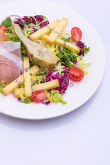 European cuisine dish salad from vegetables, cheese and ham. food on a white plate and a top view of a light background