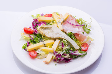 mix salad with fresh vegetables and cheese on a white plate. cherry tomato salad, lettuce, marinated artichoke, onion, cheese, ham
