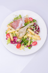 mix salad with fresh vegetables and cheese on a white plate. cherry tomato salad, lettuce, marinated artichoke, onion, cheese, ham