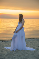Fototapeta na wymiar Beautiful girl in a long white dress walking on the seaside.
