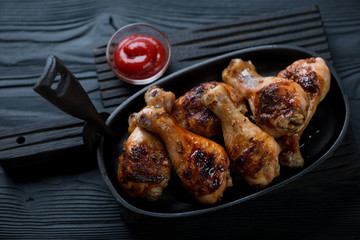 Frying pan with bbq chicken legs over black wooden background