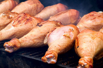 Fresh turkey drumsticks grilling on charcoal stove with fire and smoke, selective focus
