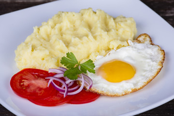 Mashed potatoes with fried eggs and tomato.