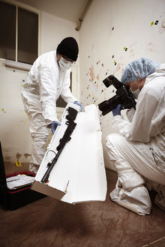 Technician and photographer packing shotgun on place of crime for laboratory testing
