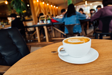 Latte art coffe with leaves texture in white cup on wooden table