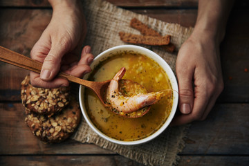 Close-up of human hands with wooden spoon eating seafood soup. Traditional asian cuisine. 