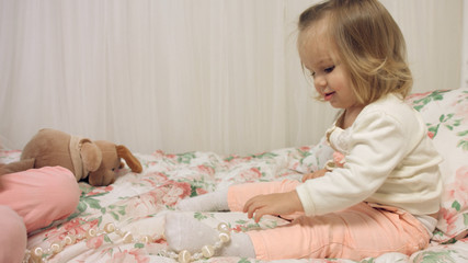 Cheerful little girls playing with beads on a bed