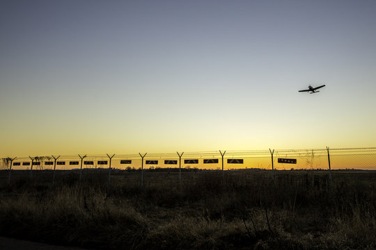 Flugzeug fliegt über den Zaun eines Flugplatzgeländes im winterlichen Sonnenuntergang