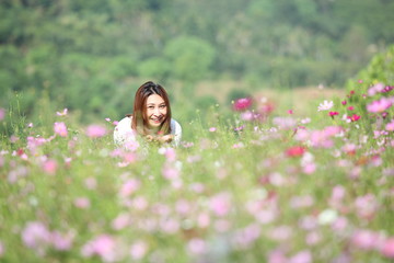 Beautiful young woman in a field of Purple, pink, red, cosmos flowers in the garden with blue sky and clouds background in vintage style soft focus.