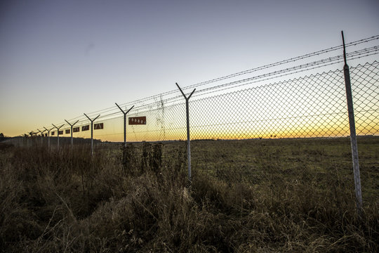 Zaun mit Hinweistafeln um ein Flugplatzgelände im winterlichen Sonnenuntergang