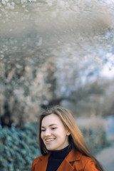 girl in a red jacket and black turtleneck with flowing hair on the background of a blossoming tree in the spring  