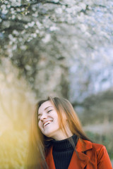 Fototapeta premium girl in a red jacket and black turtleneck with flowing hair on the background of a blossoming tree in the spring 