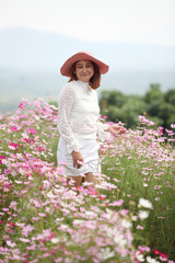 Beautiful young woman in a field of Purple, pink, red, cosmos flowers in the garden with blue sky and clouds background in vintage style soft focus.