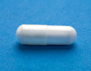 Close up one white capsule of medications on blue  background. High resolution product. Health care concept