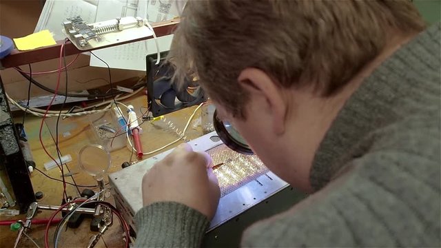 Engineer preparing new chip processor for installation on motherboard of smartphone iphone. White man in old workshop
