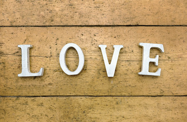 Letters spelling 'love' on wooden textured background. Old wooden floorboards are the background letters are colored white and in capitals