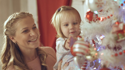 Mother with adorable baby decorate a Christmas tree at home
