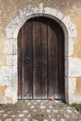 Fototapeta na wymiar Dark wooden door with arch in old stone wall