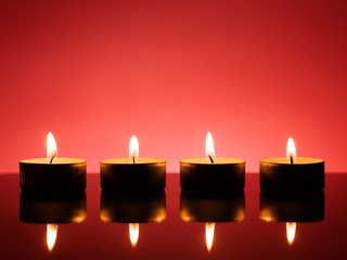 four burning tea lights on red reflective glass surface.