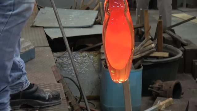 Footage of glassblowing workshop factory glassblower also known as glassmith or gaffer putting vase in wooden mall for cooling down glass is glowing yellow orange from heat and smoking by cool down 4k