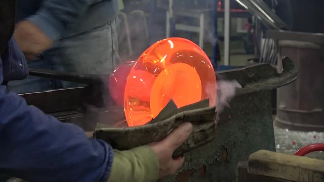 Footage of glassblowing workshop factory glassblower also known as glassmith or gaffer working on vase sanding it and blowing air into it glass crystal from oven is glowing yellow orange from heat 4k