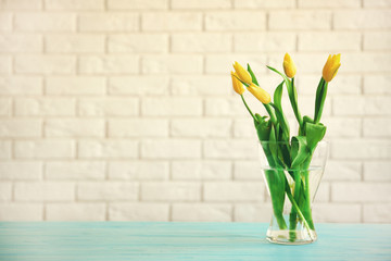 Glass vase with bouquet of beautiful tulips on brick wall background