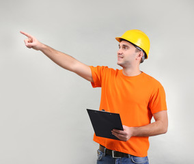 Handsome warehouse worker with clipboard pointing at something, on light background