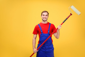 Handsome young worker with paint roller on yellow background