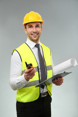 Handsome engineer with portable radio transmitter, drawing and clipboard on light background