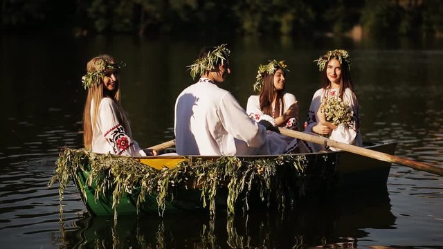 three girls and a guy in the Slavic national dress floating in a boat. Girls in wreaths in a boat. national tradition. embroidery. guessing in the summer solstice
